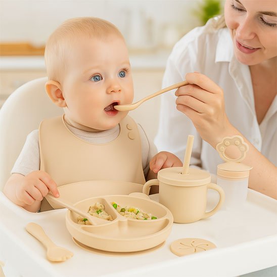 Maman nourrissant son bébé avec un set de vaisselle en silicone beige incluant assiette compartimentée, bol à ventouse et bavoir, moment de repas parent et enfant