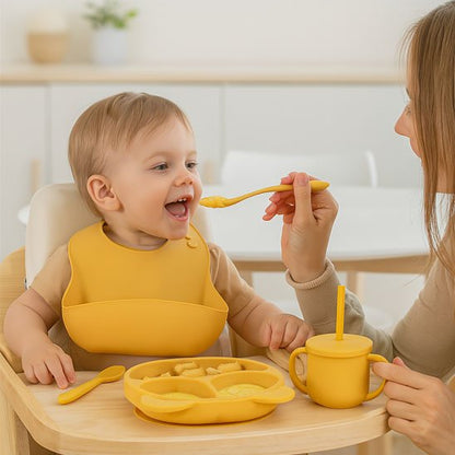 Maman nourrissant son bébé avec une cuillère en silicone jaune, set de vaisselle complet avec assiette compartimentée et tasse, moment de complicité parent-enfant
